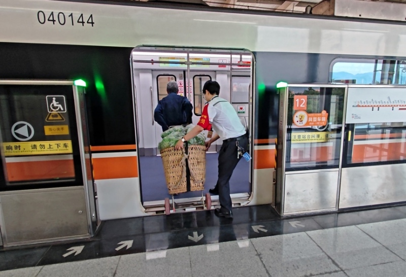 工作人员帮菜农将背篓运进地铁车厢。重庆轨道四号线建设运营有限公司供图